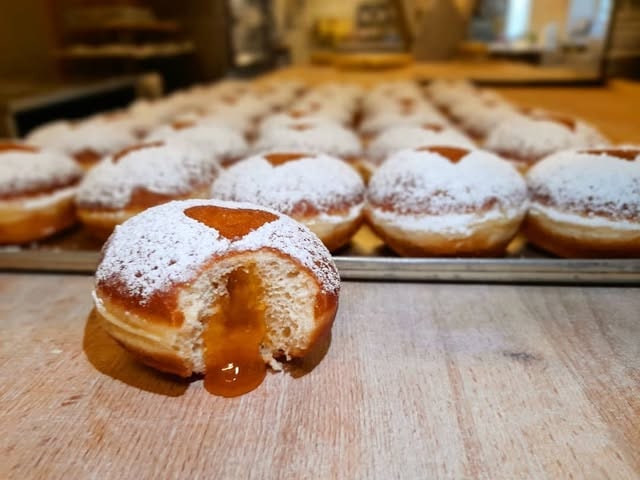 Frische Krapfen mit Staubzucker, einer aufgeschnitten mit Marillenmarmelade